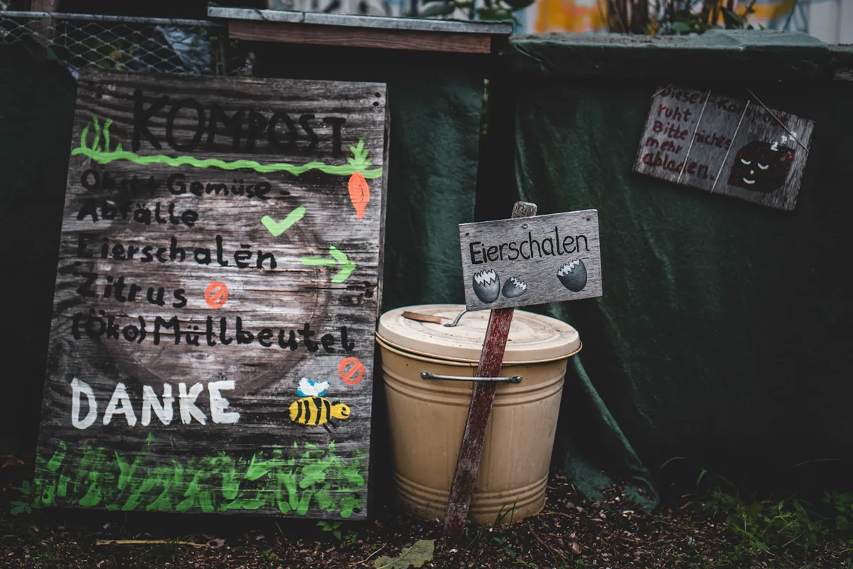 A garden compost pail beside a sign marked “COMPOST” and a small eggshell sign
